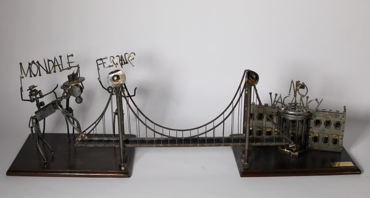 1984.31701.01_v01.jpg A metal sculpture of a bridge connecting two wooden bases. The base on the left side has three figures representing Mondale and Mrs. Ferraro, along with a donkey attempting to cross the bridge. Above the figures are the words "Mondale and Ferraro."
