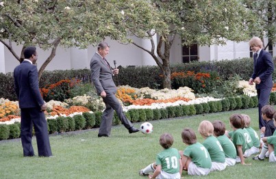 President Reagan kicking a soccer ball during a demonstration with children and Pele and Steve Moyers in the rose garden. 10/14/1982.