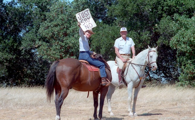 Nancy Reagan holds up a “Just Say No” sign for distant press photographs while riding with President Ronald Reagan at Rancho del Cielo, California dated 09/06/1986