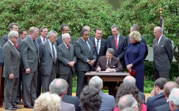 President Ronald Reagan at the signing ceremony for Executive Order 12595 establishing a White House Conference for a Drug Free America with Lois Herrington, Edwin Meese, William Bennett Samuel Pierce, George Shultz, Orrin Hatch, Benjamin Gilman, James Baker, John Herrington, Drew Lewis, Otis Bowen, Ted Stevens, and Charles Rangel in the Rose Garden dated 05/05/1987