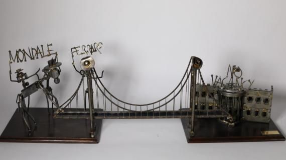 A metal sculpture of a bridge connecting two wooden bases. The base on the left side has three figures representing Mondale and Mrs. Ferraro, along with a donkey attempting to cross the bridge. Above the figures are the words "Mondale and Ferraro."