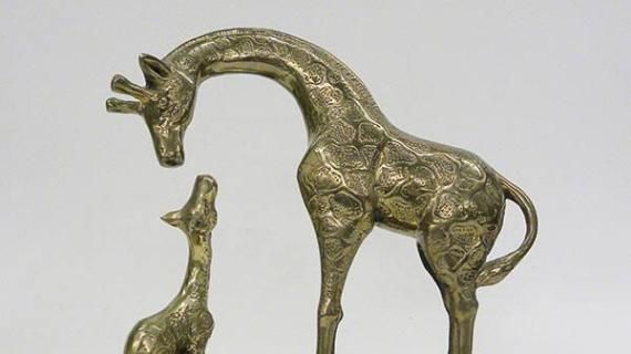 This is a sculpture of two brass giraffes, one large and the other small. The larger giraffe is craning its neck down toward the smaller giraffe, which is looking up toward it. The giraffes are mounted on a wooden base with a brass plaque stating "NANCY REAGAN 'FOR STICKING YOUR NECK OUT FOR KIDS', NATIONAL FEDERATION OF PARENTS FOR DRUG-FREE YOUTH, SEPTEMBER 28, 1984." Nancy Reagan attended the third annual National Federation of Parents NFP luncheon on 09/28/1984.