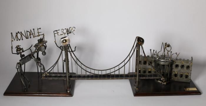 A metal sculpture of a bridge connecting two wooden bases. The base on the left side has three figures representing Mondale and Mrs. Ferraro, along with a donkey attempting to cross the bridge. Above the figures are the words "Mondale and Ferraro."