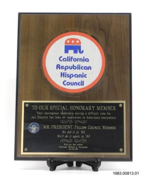 A wooden plaque with a metal disk with text stating, "California Republican Hispanic Council" and "To our special honorary member, your courageous leadership during a difficult time for our country has been an inspiration to Americans everywhere, Mr. president, fellow council member, we did it in '80, we'll do it again in '84, with our best wishes."