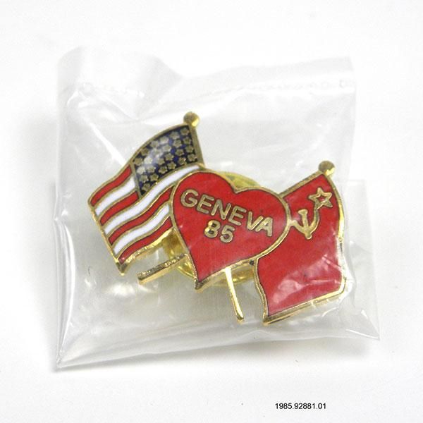 Geneva 85 Pin: A plastic bag with a lapel pin depicting the U.S. flag and the U.S.S.R. flag joined by a heart with text stating “Geneva 85.”