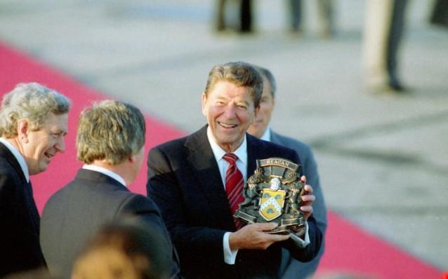 President Ronald Reagan receiving gift of Reagan coat of arms at his arrival ceremony at Shannon Airport in Ireland with President Patrick Hillery and Prime Minister Garret FitzGerald 06/01/1984 C22220-26A
