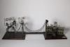 A metal sculpture of a bridge connecting two wooden bases. The base on the left side has three figures representing Mondale and Mrs. Ferraro, along with a donkey attempting to cross the bridge. Above the figures are the words "Mondale and Ferraro." The right base features the White House with the words "No Vacancy" above it. The front corner of the base has a mall brass tone plaque with the text "IF IT DON'T NEED FIXIN'- DON'T FIX IT."