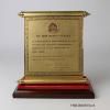 A gold-toned metal scroll (b) mounted on a wooden base (a) The text on the scroll states "TO MRS. NANCY REAGAN IN APPRECIATION OF YOUR UNTIRING EFFORTS TO ESTABLISH EFFECTIVE INTERNATIONAL COOPERATION IN THE PREVENTION OF DRUG ABUSE. GIVEN THIS 4TH DAY OF MAY NINETEEN HUNDRED AND EIGHTY SIX IN BANGKOK, THAILAND GENERAL PREM TINSULANONDA PRIME MINISTER OF THAILAND." At the top of the scroll is an "OFFICE OF THE NARCOTICS CONTROL BOARD" emblem. 