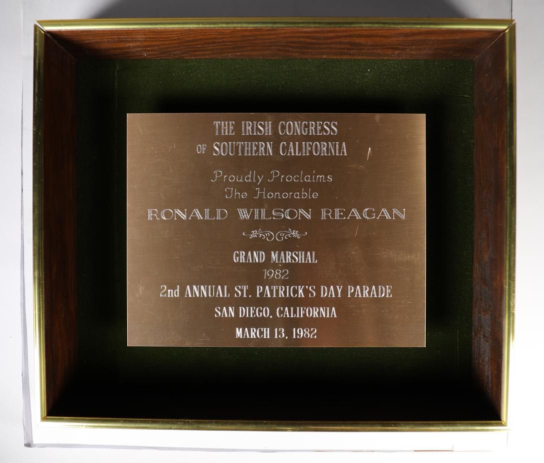 A copper-colored metal plaque set into a wooden shadowbox frame with a green felt background. The plaque states “THE IRISH CONGRESS OF SOUTHERN CALIFORNIA Proudly Proclaims The Honorable RONALD WILSON REAGAN GRAND MARSHAL 1982 2ND ANNUAL ST. PATRICK’S DAY PARADE SAN DIEGO, CALIFORNIA MARCH 13, 1982.” Gifter: Larry Barnes. Artifact ID: 1982.00416.01
