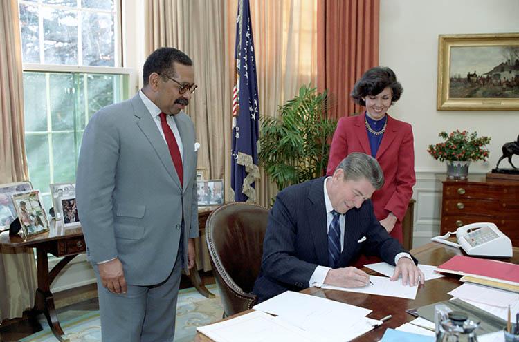 President Ronald signing the United States Commission on Civil Rights Act of 1983, re-establishing the Commission on Civil Rights as an independent, bipartisan, eight-member federal agency, with Staff Director of the Commission Linda Chavez and Chairman Clarence Pendleton in the Oval Office (as enacted H.R. 2230 is Public Law 98-183) 11/30/1983 NAID: 75853149