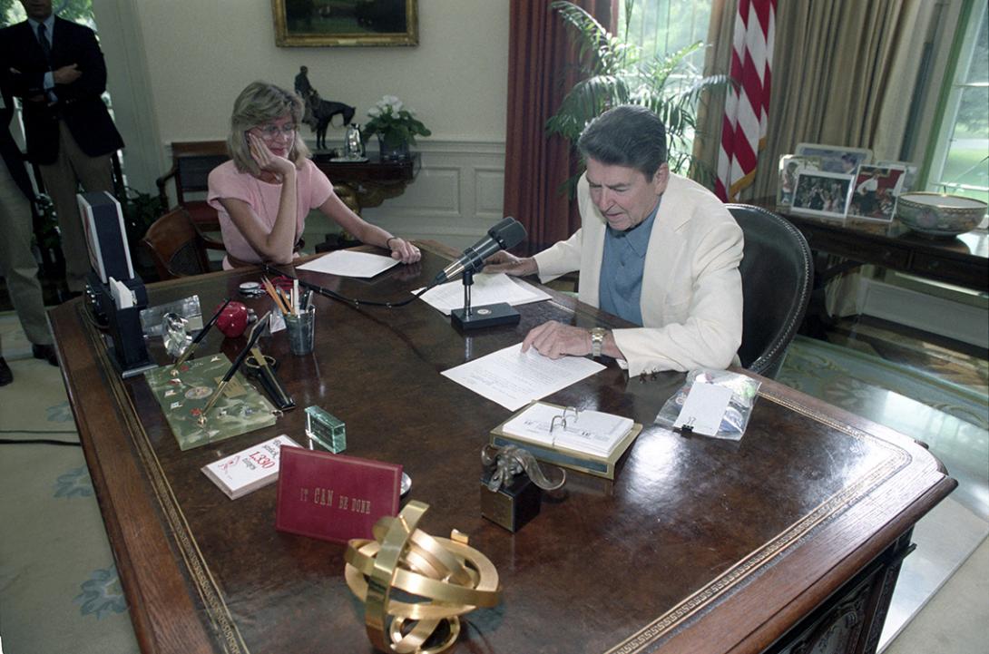  President Ronald Reagan delivering his Radio Address to the Nation on the Observance of Labor Day with media coordinator Janice Mahan-Duvall in the Oval Office 09/01/1984  NAID: 404525181