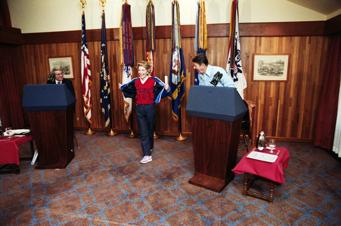 Nancy Reagan showing off her “4 more in ‘84” sweater during debate preparation for the upcoming debate on domestic policy between President Reagan and David Stockman (as Walter Mondale) at Camp David 10/06/1984 NAID: 75853649
