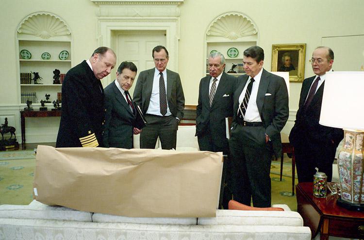 President Ronald Reagan meeting in the Oval Office with staff regarding the Libya air strike Left to right: Admiral Crowe, Secretary of Defense Caspar Weinberger, Vice President George Bush, Chief of Staff Donald Regan, and Assistant to the President for National Security Affairs John Poindexter 03/24/1986 NAID: 75854689