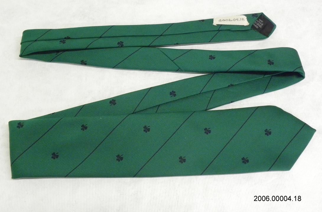 A silk kelly green with narrow navy blue diagonal stripes and navy blue embroidered shamrock. The back interior is lined with navy blue fabric and has a label stating "Creative Expressions By Alynn Neckwear Stamford Conn."  Gifter: Nancy Reagan. Artifact ID: 2006.00004.18