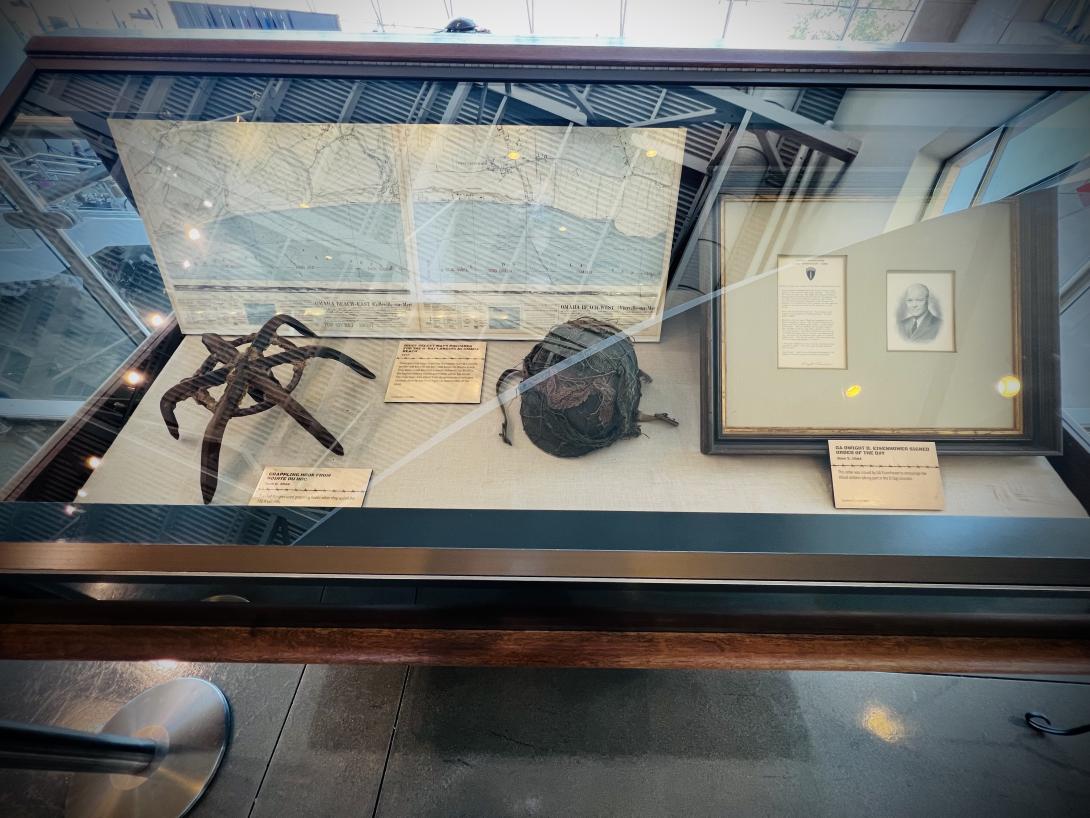 Full display of case containing items from D-Day including a helmet, grappling hood and secret maps.