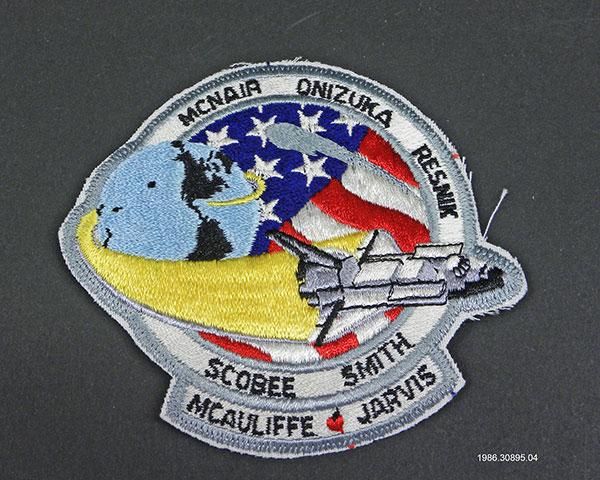  Challenger Patch Artifact ID: 30895.036 Object Name: Patch Date Made: 1986 Description: A fabric patch with an image of the Space Shuttle Challenger flying around the Earth and over the American flag. Surrounding the image are the last names: "Smith, Resnik, McNair, Onizuka, Jarvis, and McAuliffe."