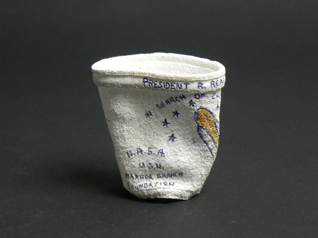 [View 1 of 5] Shrunken Challenger Coffee Cup Artifact ID: 1986.31470.01 Maker: Roger W. Cook, Director, Marine Operations, Harbor Branch Foundation Inc., Fort Pierce, Florida Date Made: 1986 Label Text: This cup was placed in the battery compartment of the submersible used by the donor's company to search for the Space Shuttle Challenger. The size of the cup was reduced under pressure at 1284 Ft.