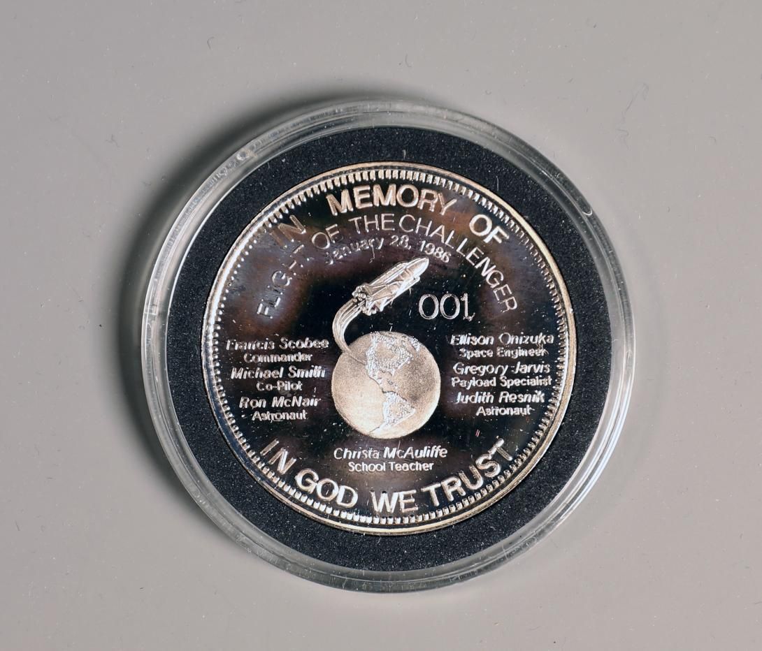 [Side 1 of 2] Challenger Commemorative Coin Artifact ID: 1987.02013.01a-b Object Name: Coin, Commemorative Maker: Dale L. Jones, Secretary-Treasurer, Silver Trust Investments Inc. Date Made: 1986.  A silver commemorative coin encased in a plastic holder for the Space Shuttle Challenger made by Donor Dale L. Jones.
