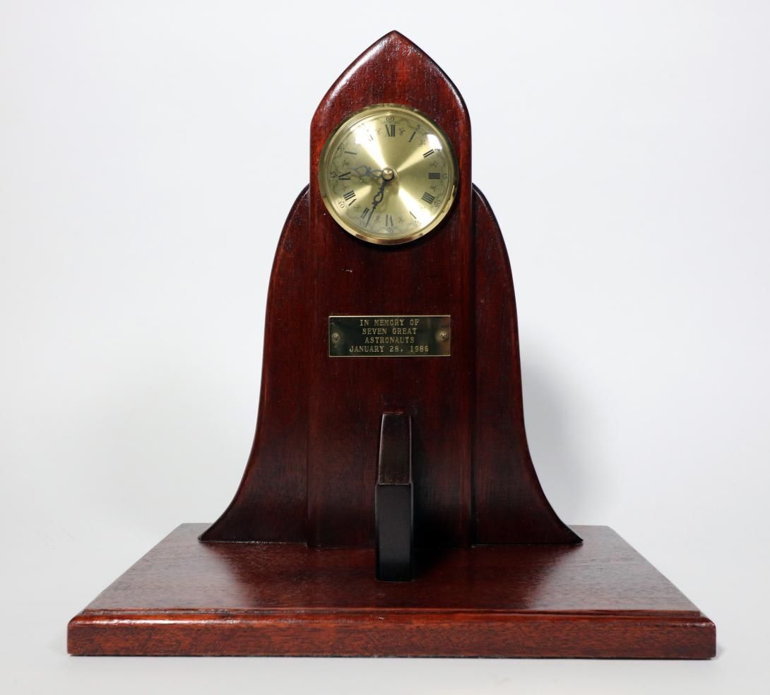 Space Shuttle Clock Artifact ID: 1986.00327.01 Object Name: Clock Date: 1986 Description: A wooden clock shaped like a space shuttle meant to represent the Challenger. At the center of the wooden design is an engraved metal plaque stating “IN MEMORY OF SEVENT GREAT ASTRONAUTS JANUARY 28, 1986.”