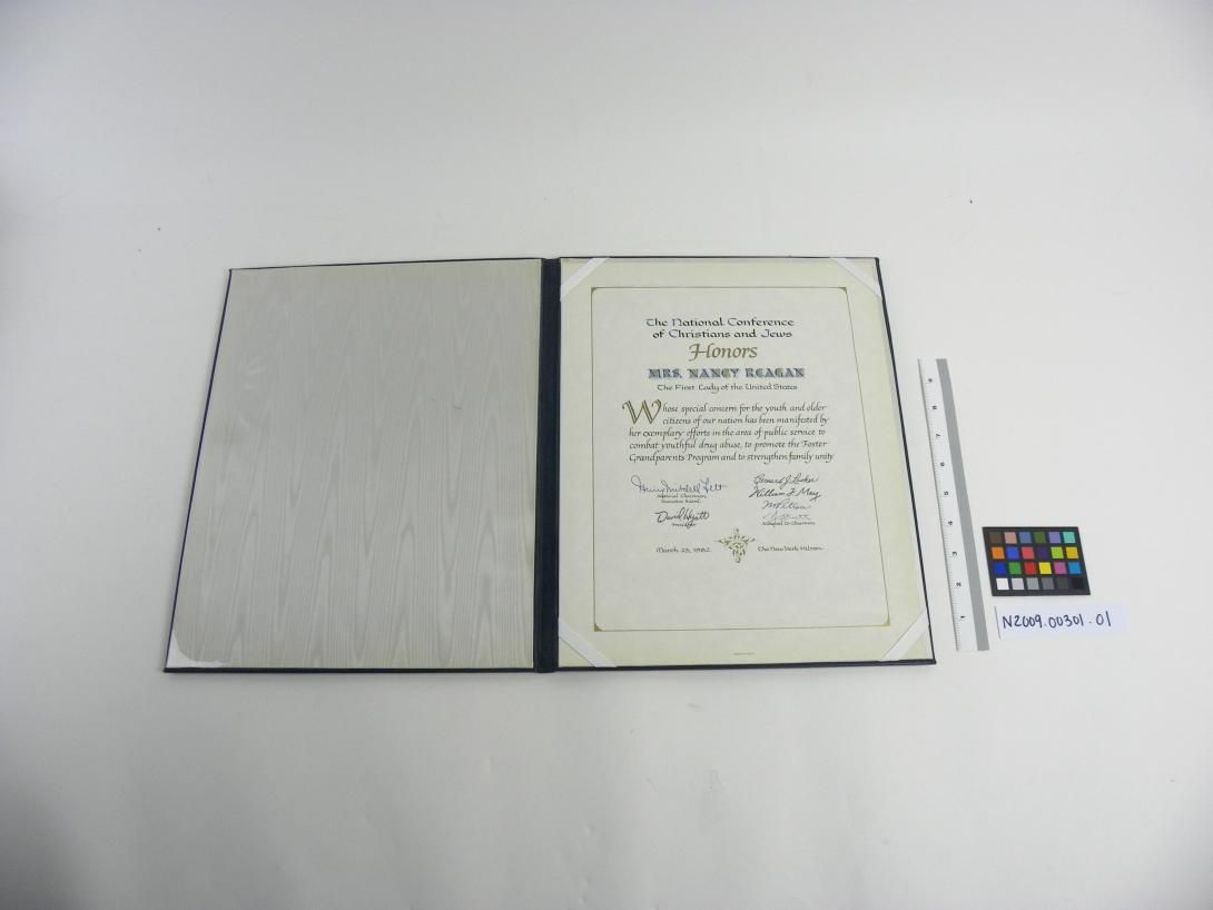 Achievement Certificate, blue leather album inside is "The National Conference of Christians and Jews Honors Mrs. Nancy Reagan the First Lady of the United States Whose special concern for the youth and older citizens of our nation has been manifested by her exemplary efforts in the area of public service to combat youthful drug abuse, to promote the Foster Grandparents Program and to strengthen family unity"