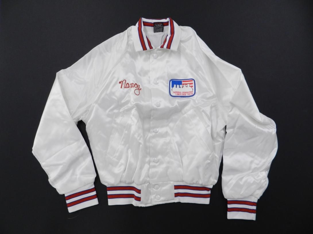 Jacket - White satin with red, white, & blue trip, lettered "Nancy" in red, with a "NFDY" Patch, at the left. Nancy Reagan attended the third annual National Federation of Parents (NFP) luncheon on 09/28/1984. There she was given this “coach’s” jacket.
